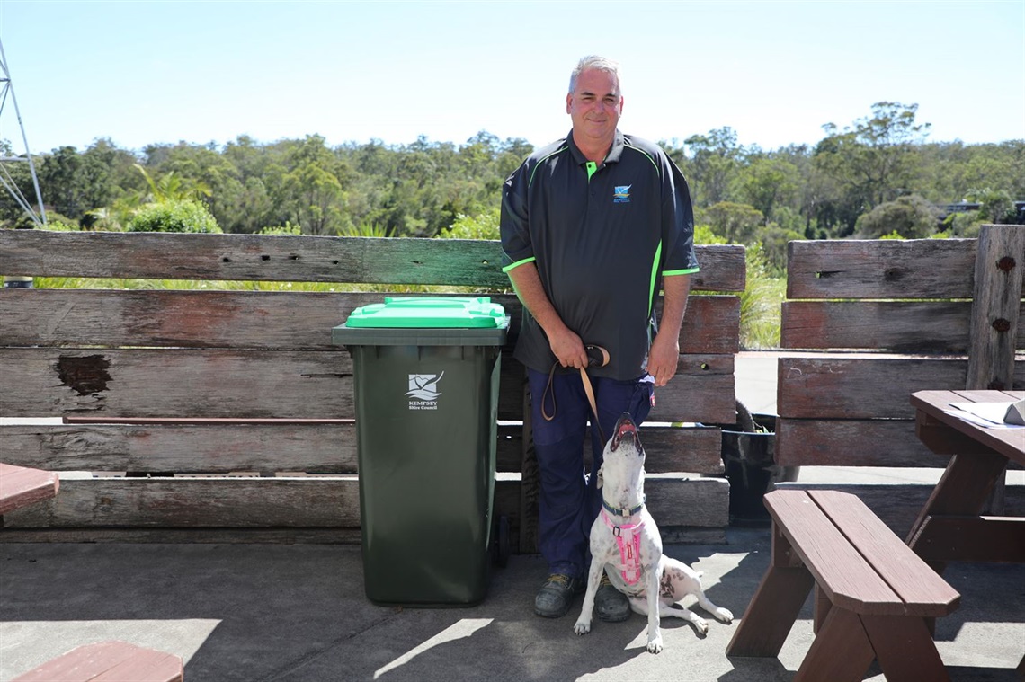 A man and a dog next to a kerbside green bin